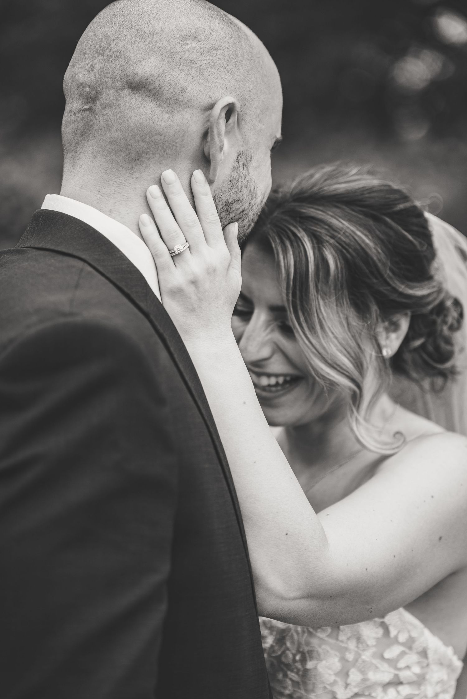 Black and white intimate moment of laughing bride embracing groom showing wedding ring.