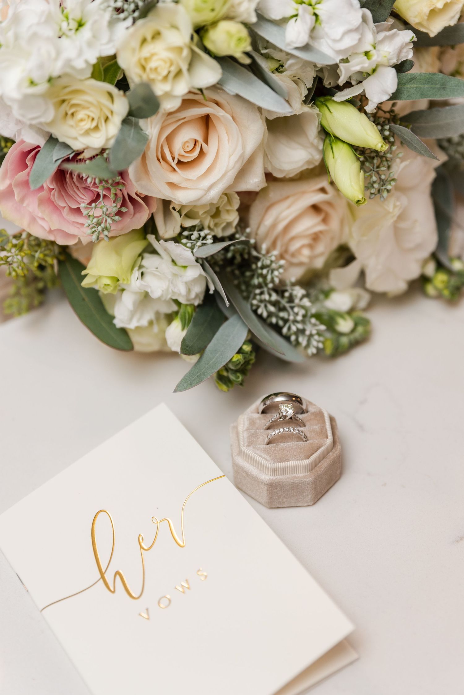 Wedding flat lay with bridal bouquet, diamond rings in velvet box, and her vows booklet.
