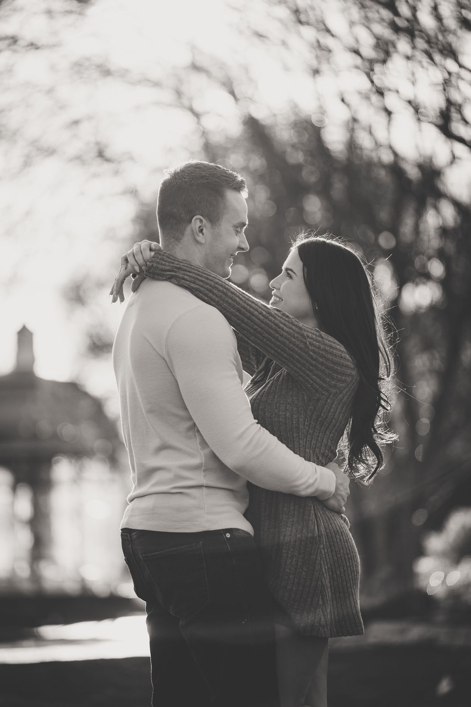 Black and white photo of a couple embracing and gazing at each other in a sunlit outdoor setting.