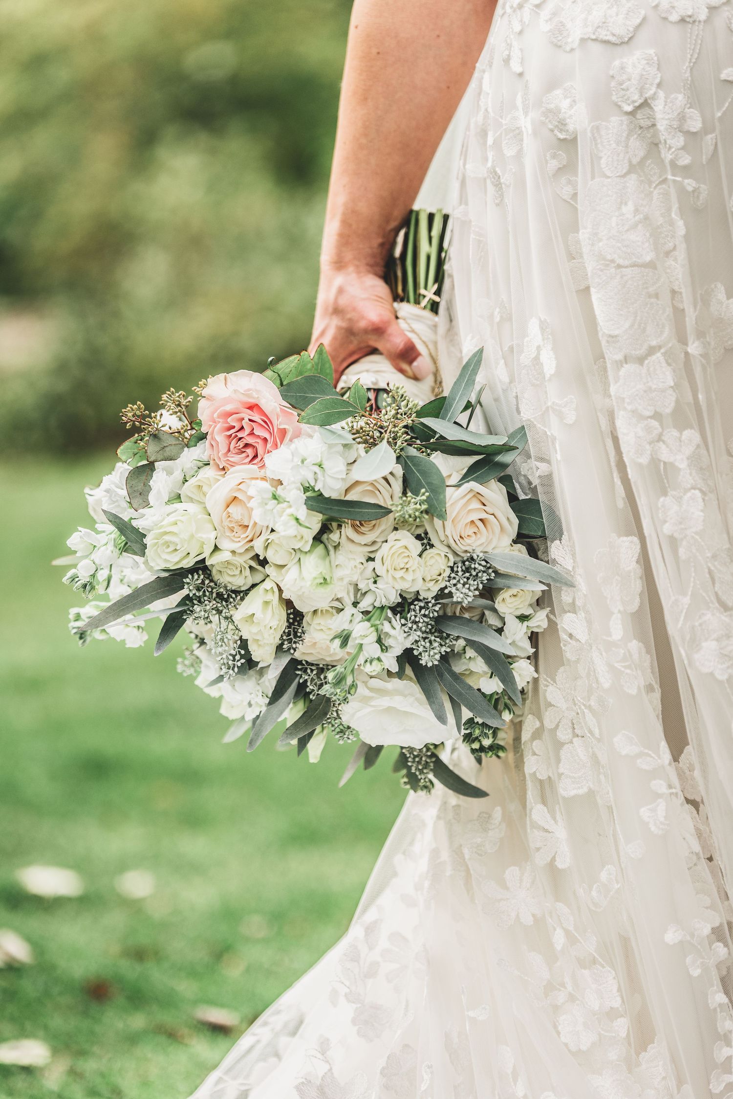 Bride in floral lace wedding gown holding elegant pink and white rose bridal bouquet.