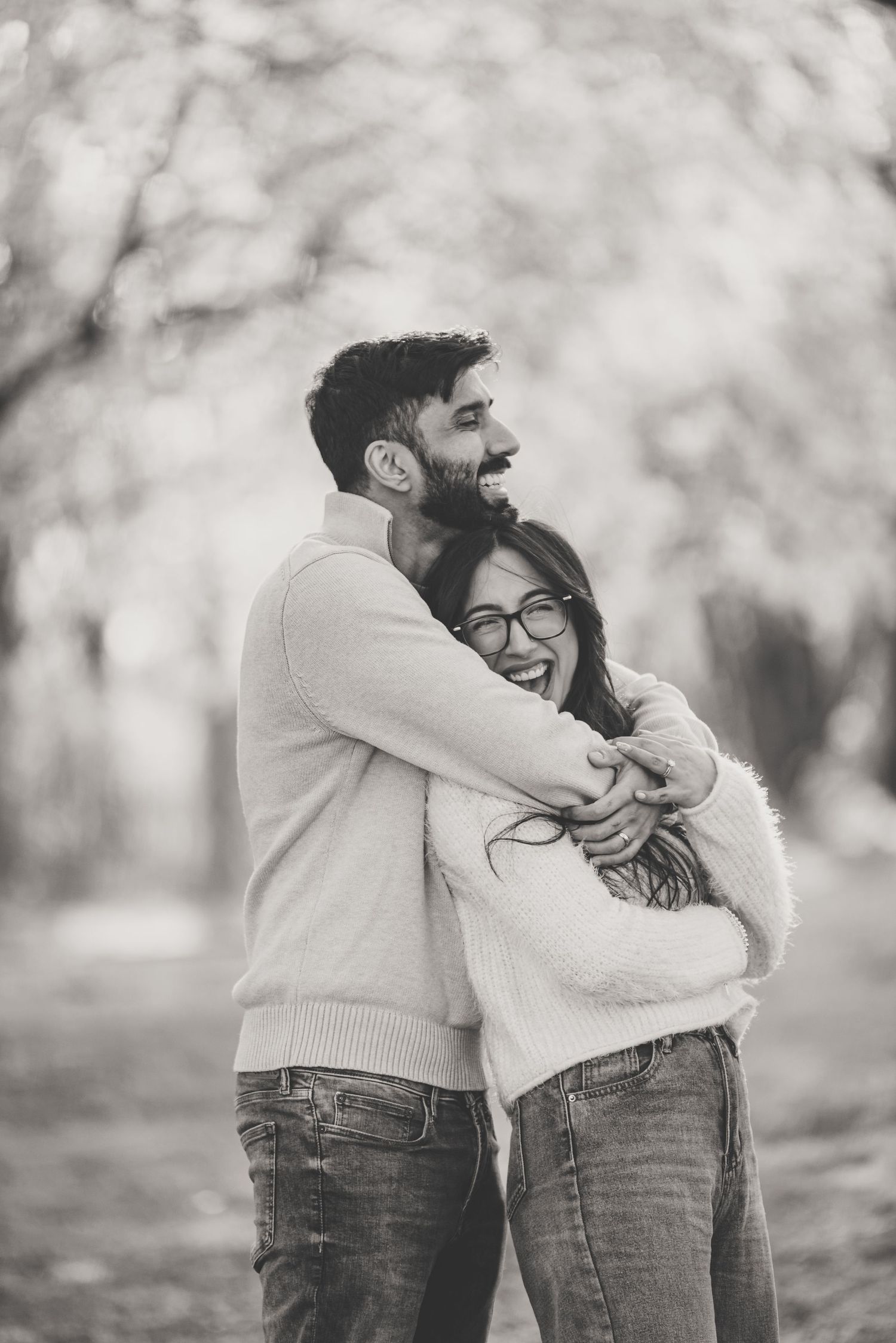 Black and white photo of joyful couple hugging and laughing together under blooming spring trees.