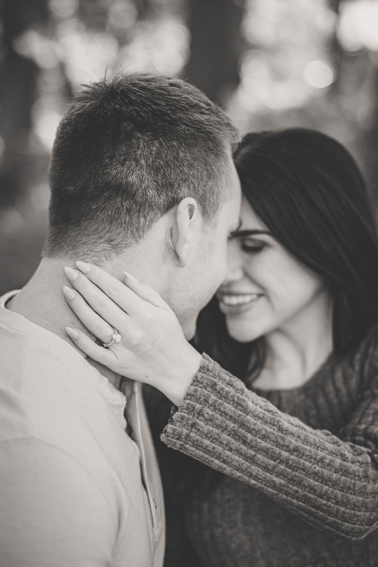 Black and white close-up of couple nearly kissing, woman smiling with engagement ring visible on hand.