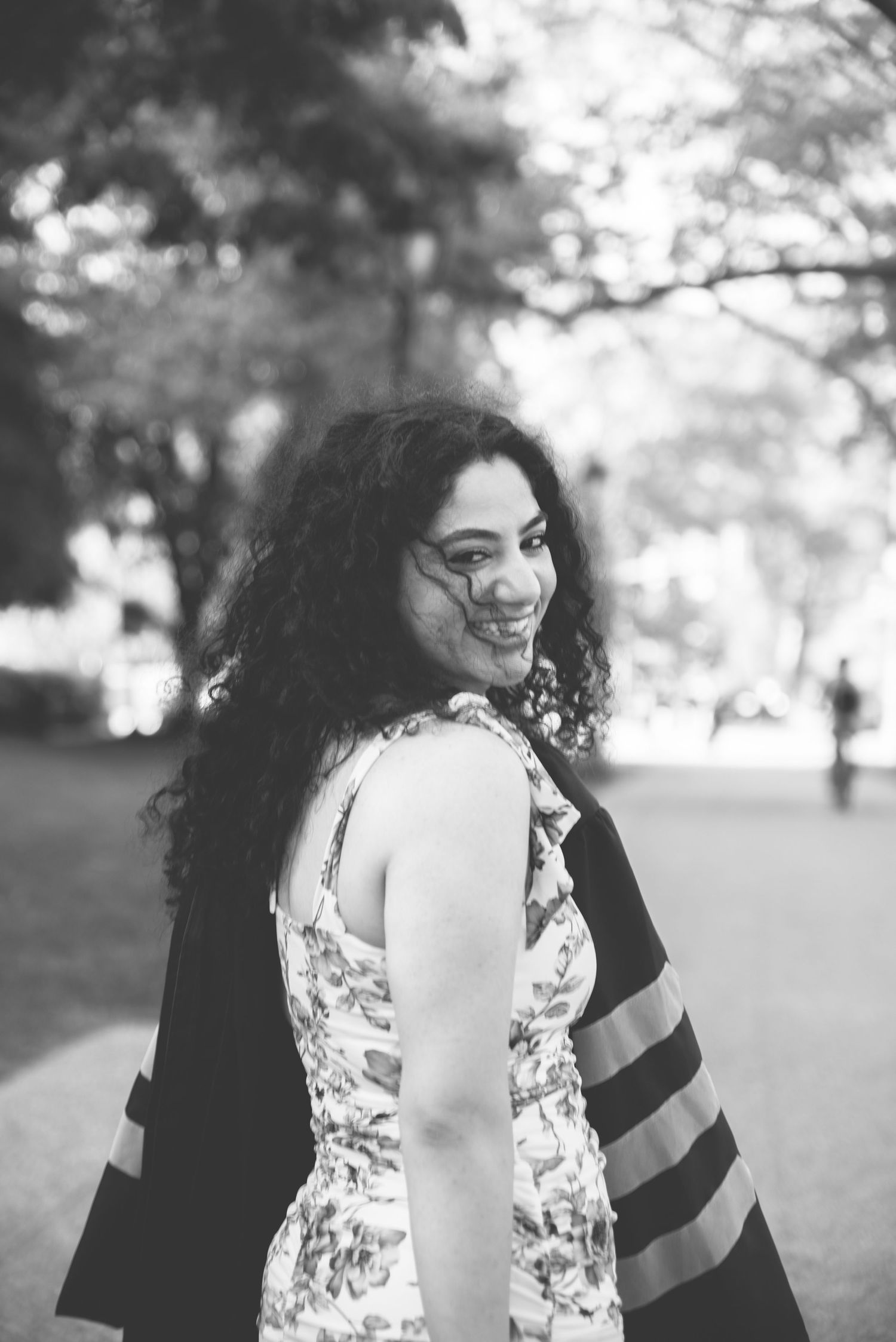 Black and white portrait of a curly-haired woman smiling over her shoulder in a park setting.