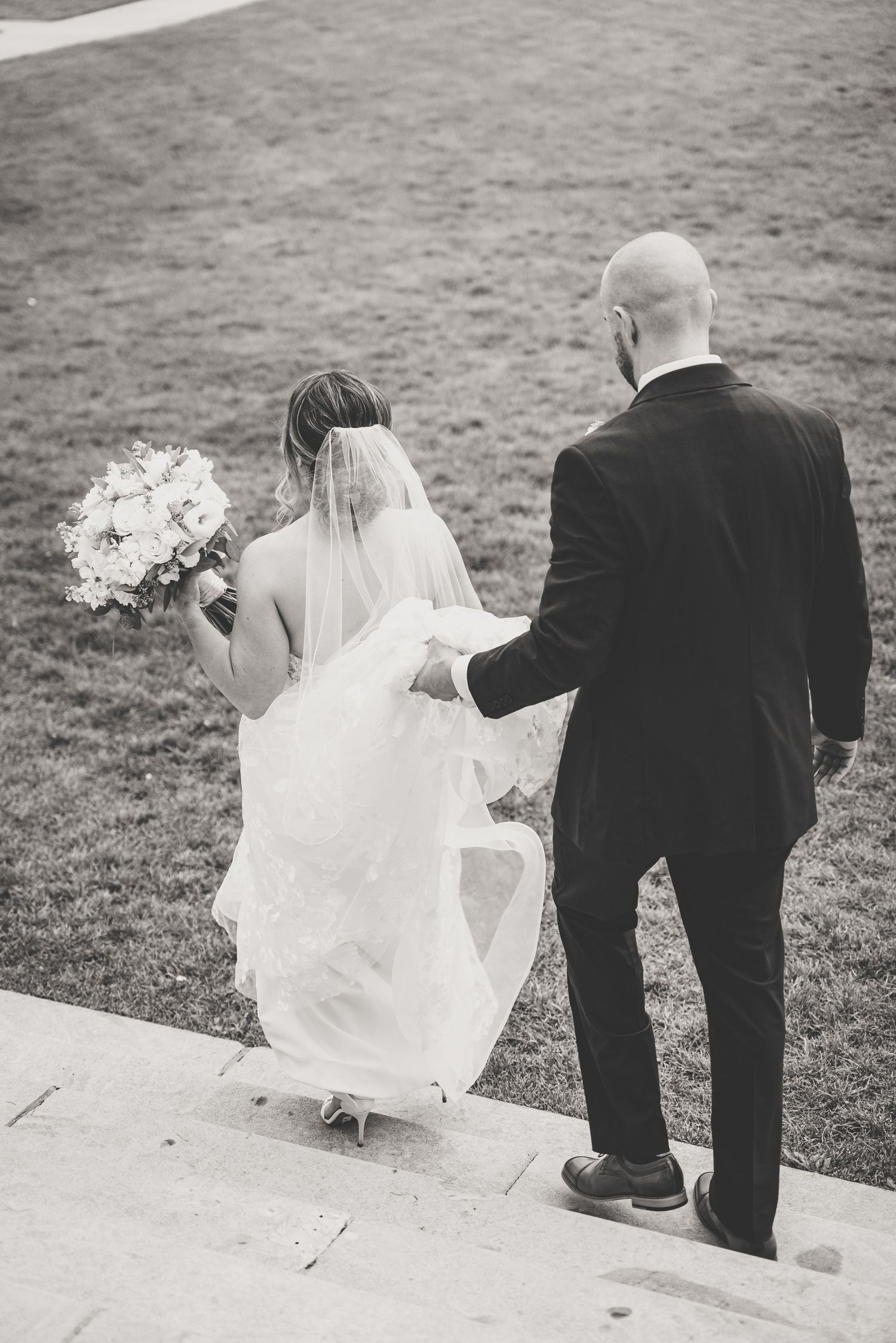 Black and white photo of bride and groom walking down steps after wedding ceremony.