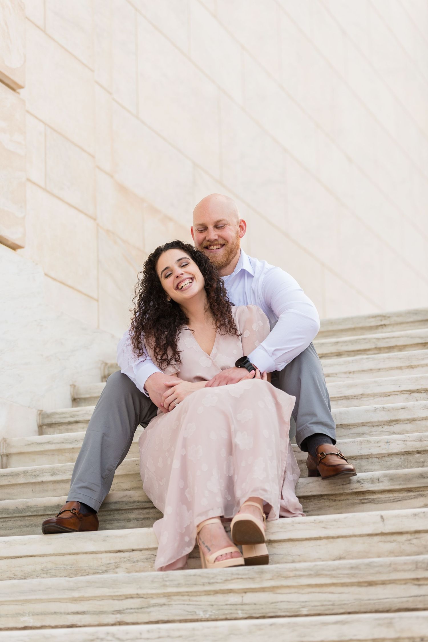 Smiling couple sitting close together on marble steps outside a large stone building.