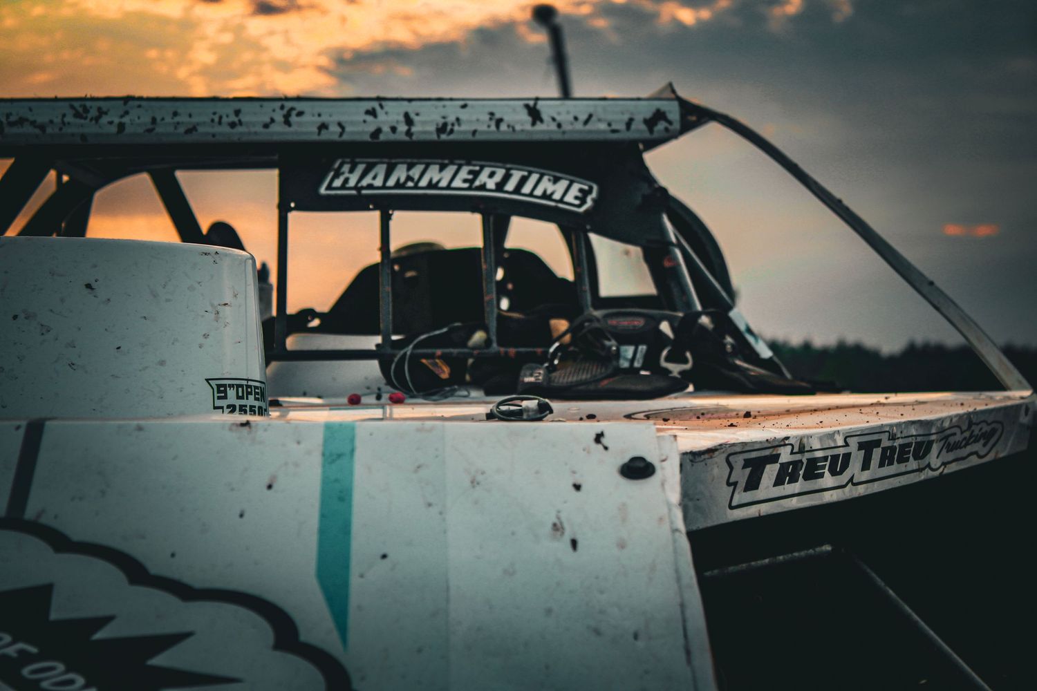 Race car silhouetted against dramatic orange sunset sky during a motorsport event.