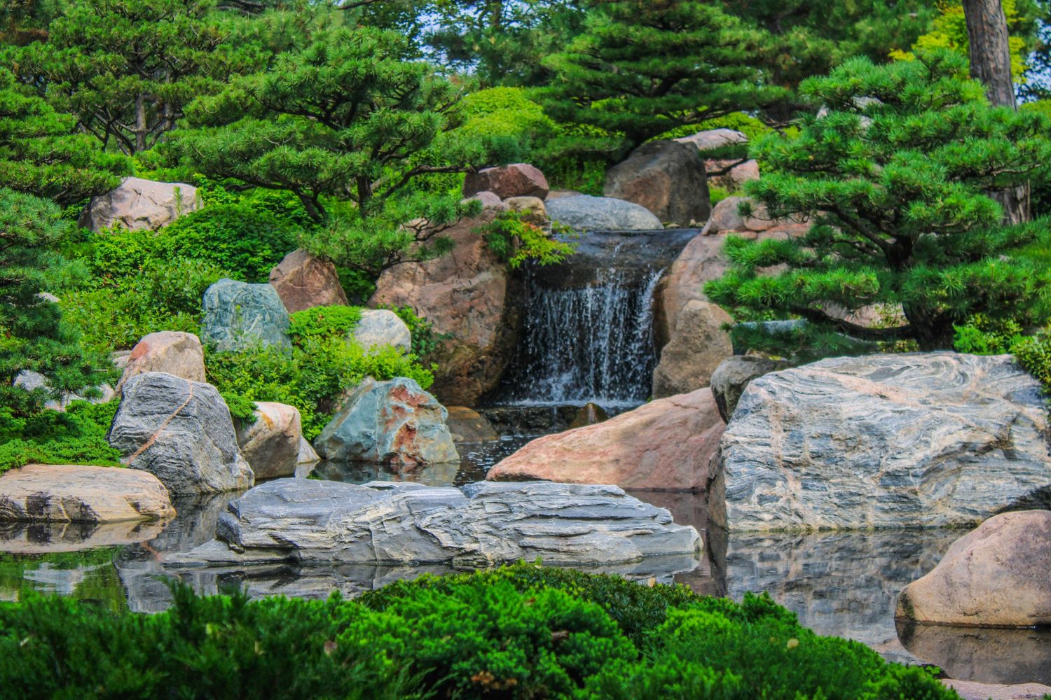 Cascading waterfall flows over rocky terrain surrounded by lush green foliage in a natural landscape setting.