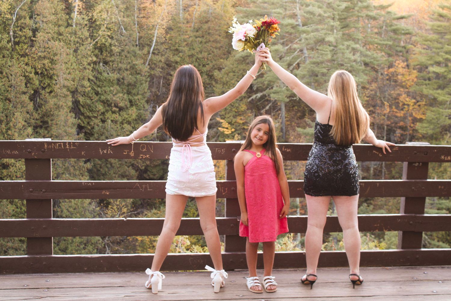 Three people pose together on a wooden deck overlooking a forest landscape at sunset.