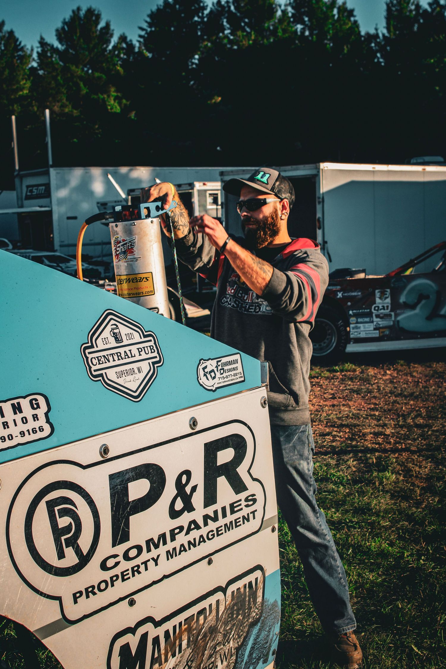 Racing car signage and decals being installed on a blue vehicle at an outdoor event.