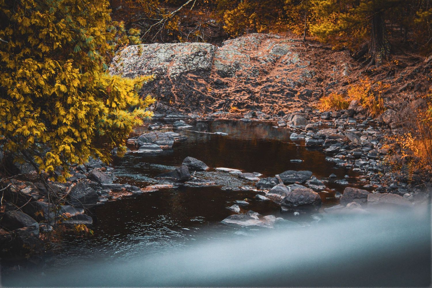 Panoramic view of rocky riverbed with autumn foliage along the banks.