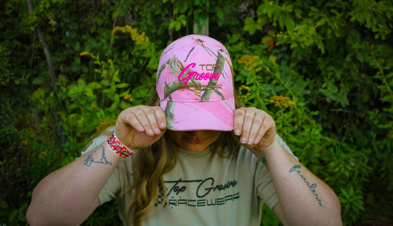Pink baseball cap with custom graphics displayed against green foliage background.