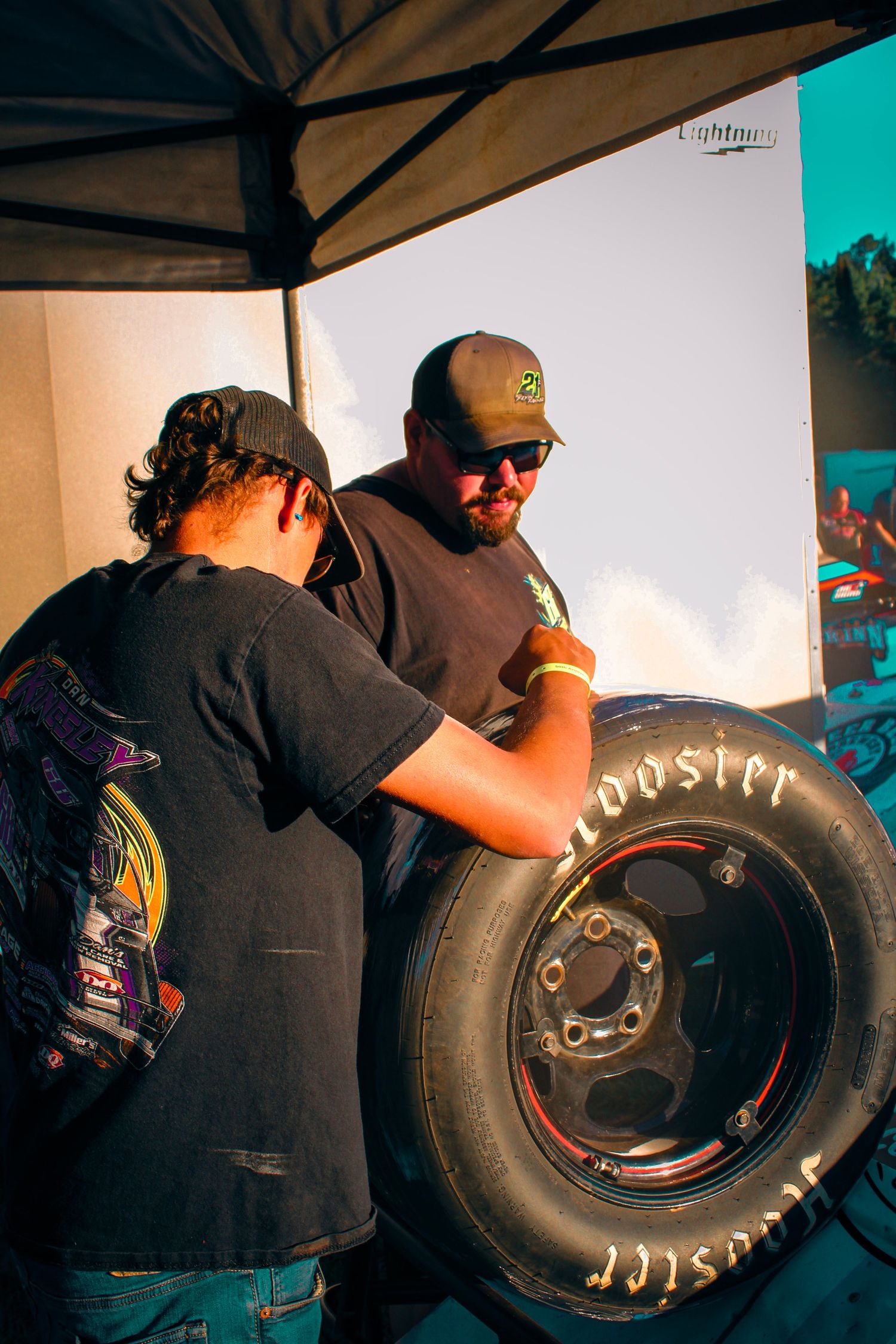 Mechanics working on large racing tires in a pit crew area.