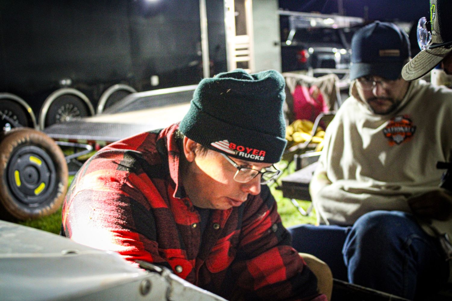 People working on projects in dimly lit workshop space with red plaid visible.