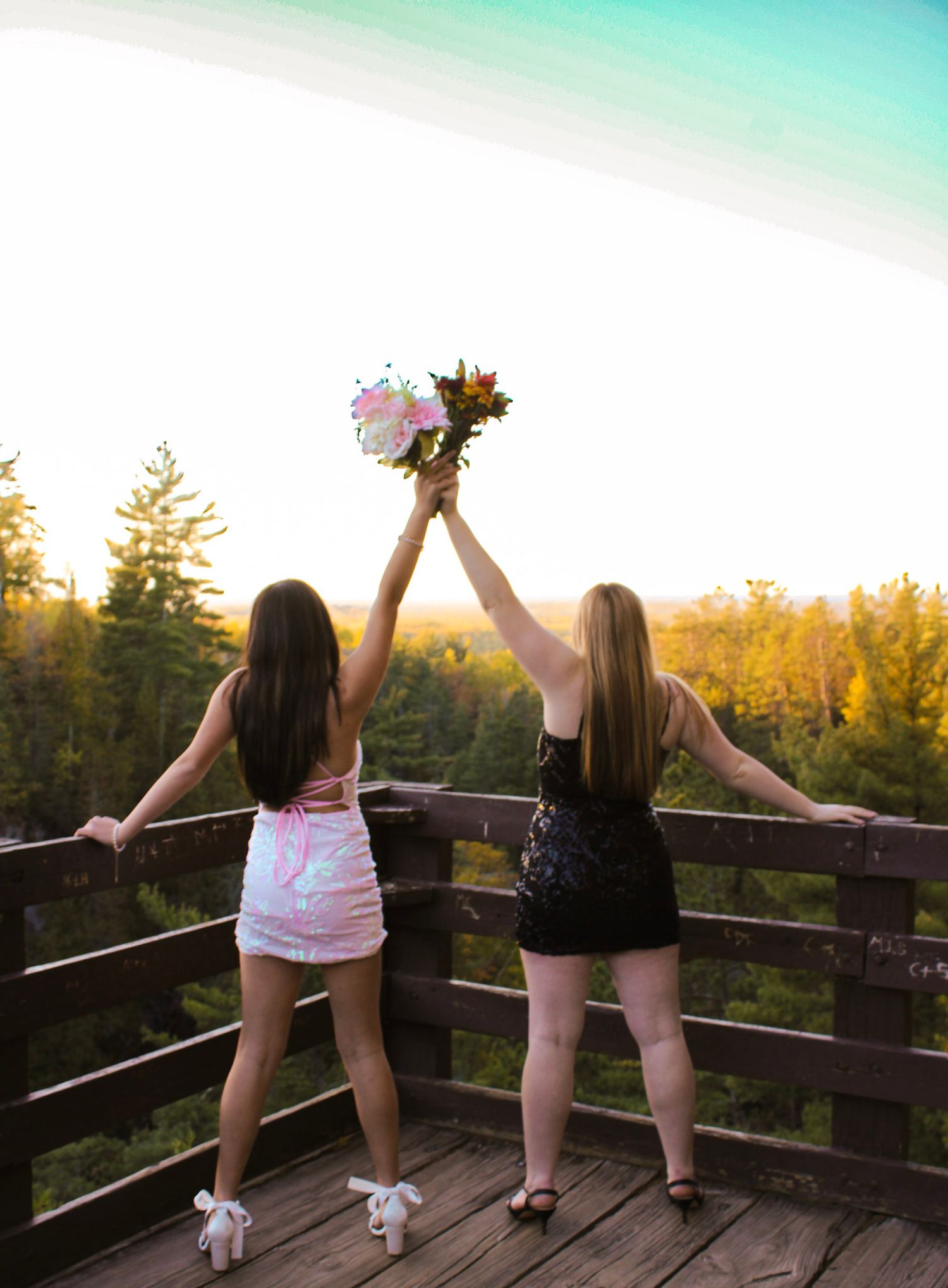 Two people celebrate with raised arms on wooden deck at sunset.