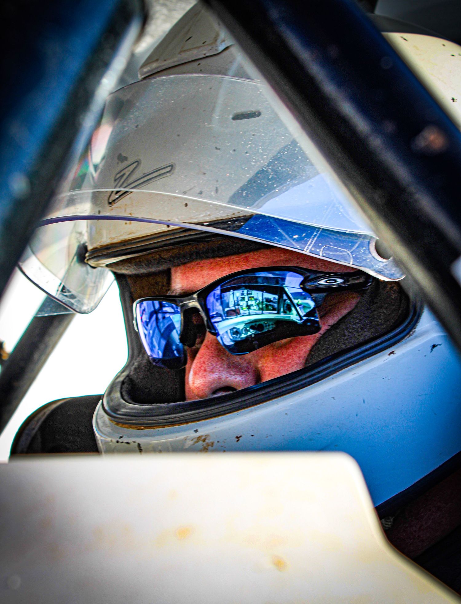 Racing helmet with reflective visor seen through a car window.