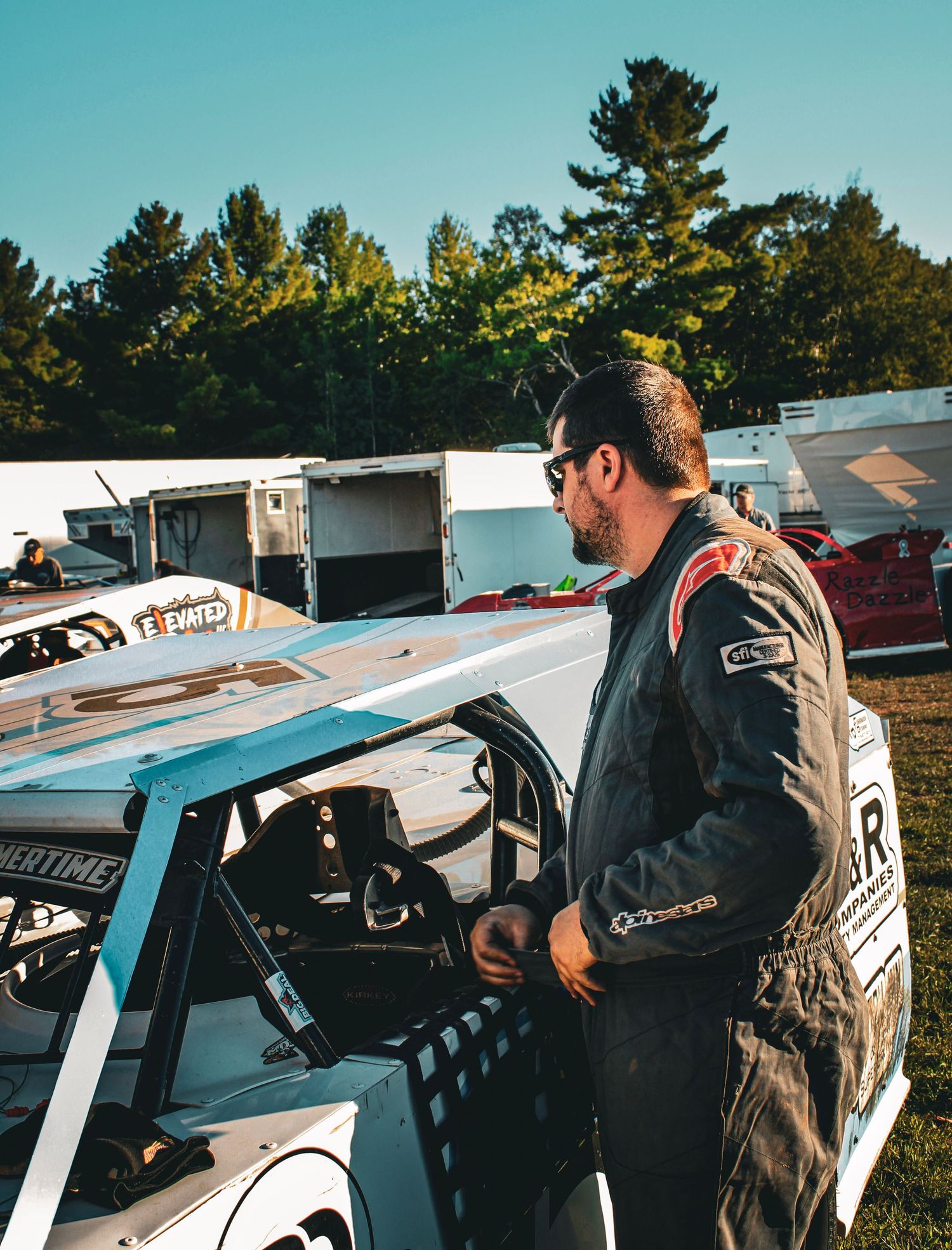 Racing driver in protective suit inspects vehicle before race at outdoor track.