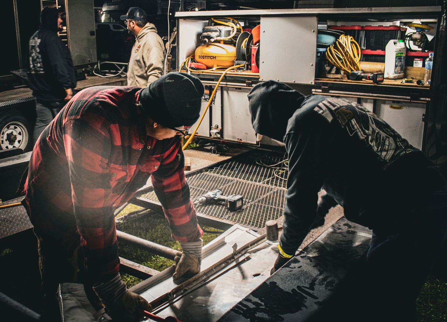 Mechanics working on race car maintenance in a dimly lit garage setting.