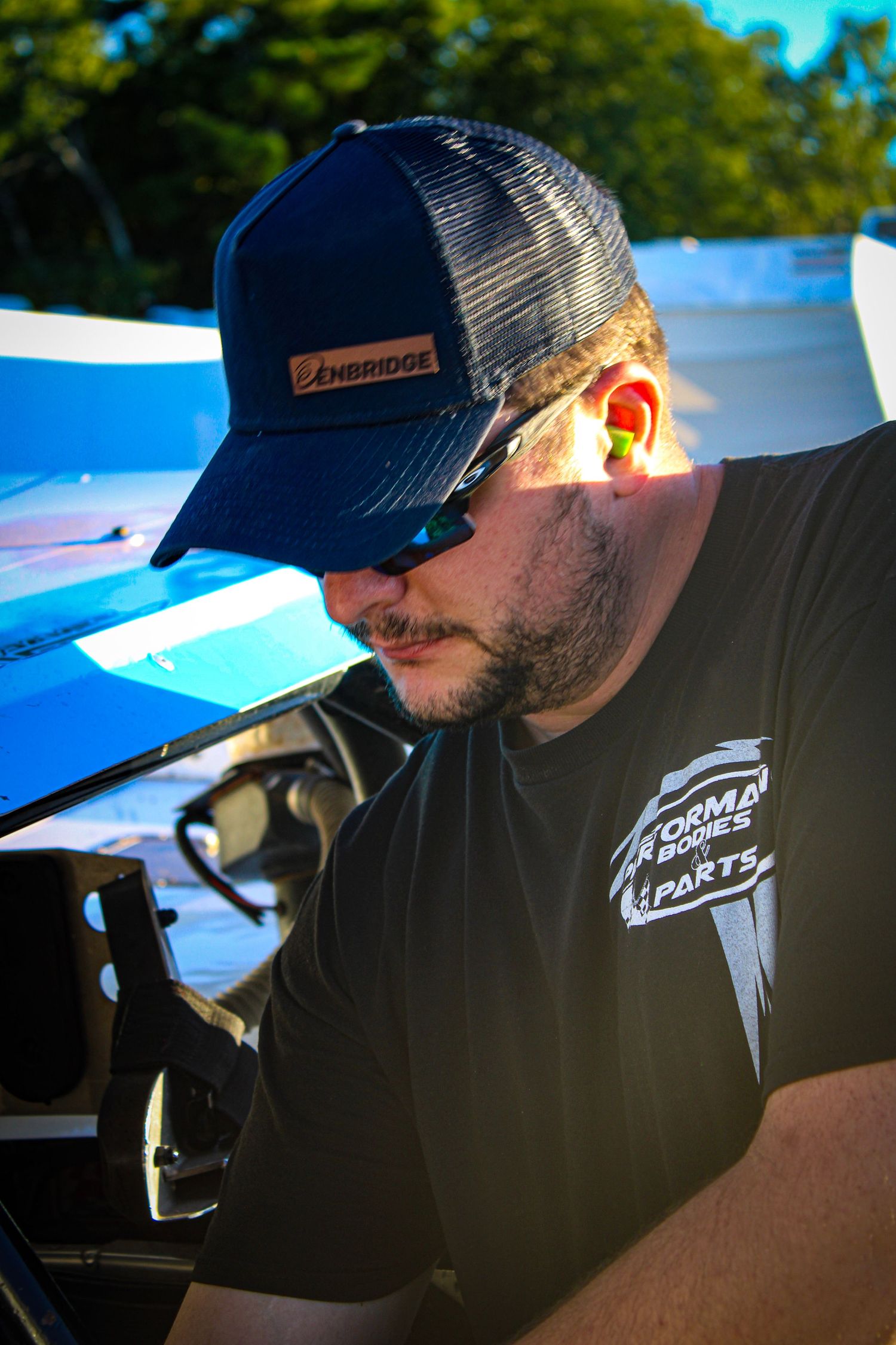 Person working on race car preparations wearing team apparel and baseball cap.