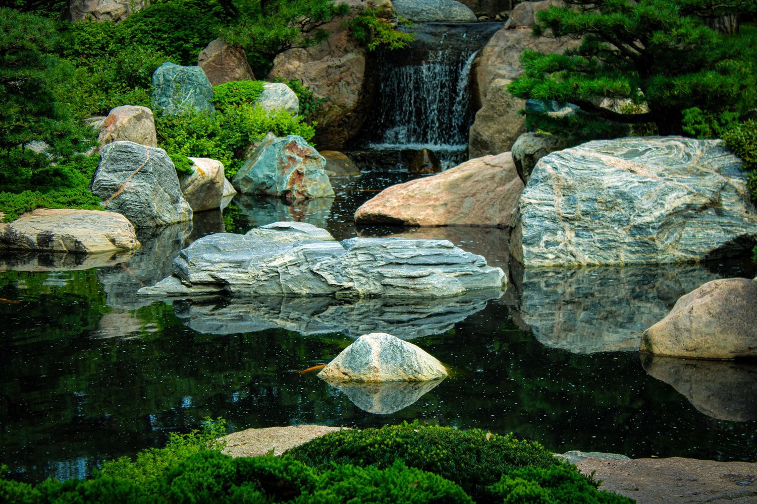 Tranquil Japanese garden pond with waterfall and carefully arranged rocks creating reflections.