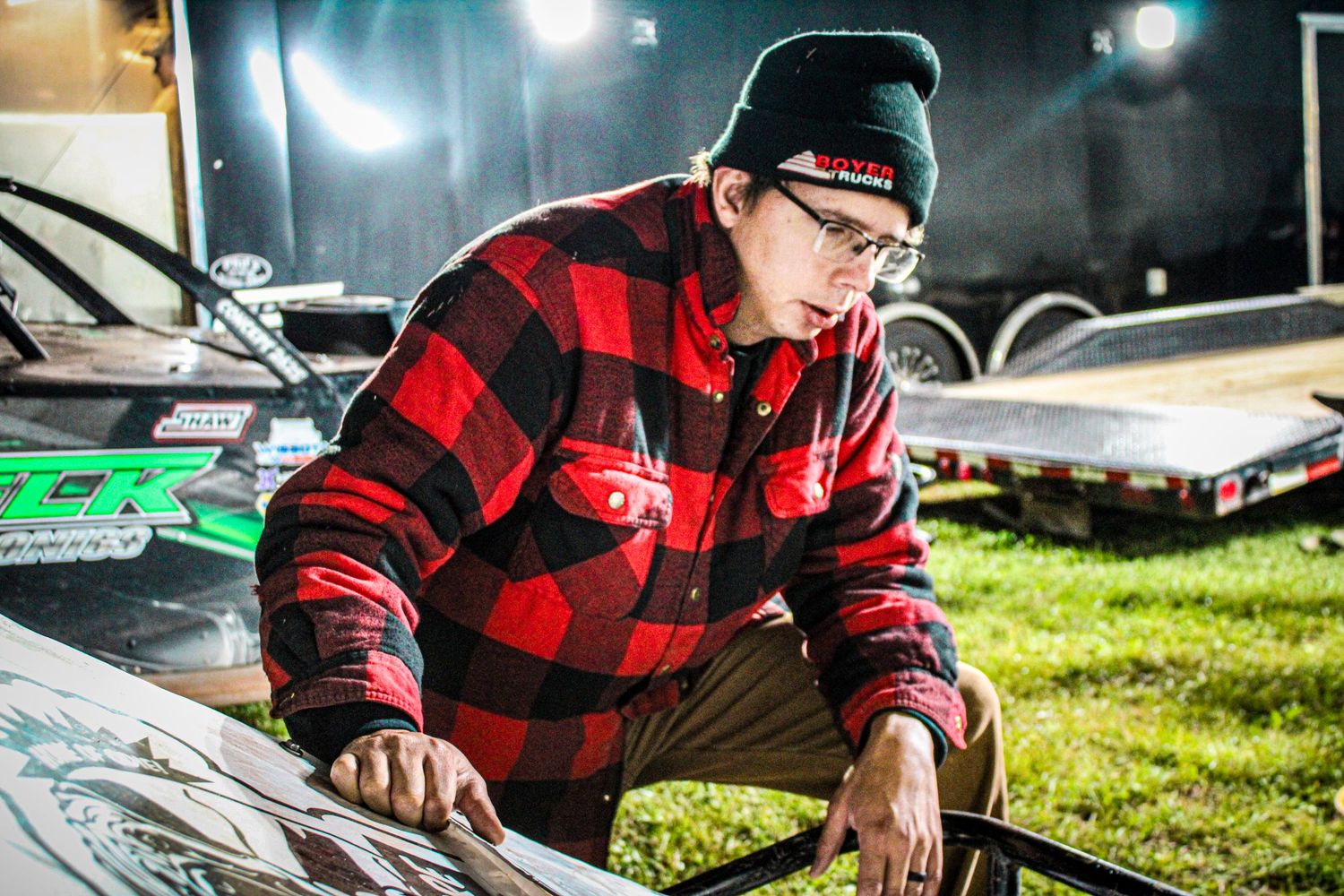 Mechanic in red plaid jacket working on equipment outdoors at night.