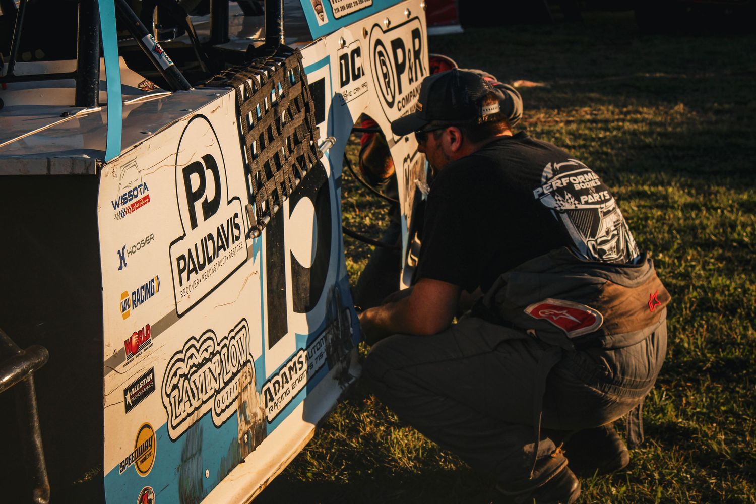 Racing team members working on vehicle preparations at an outdoor event.