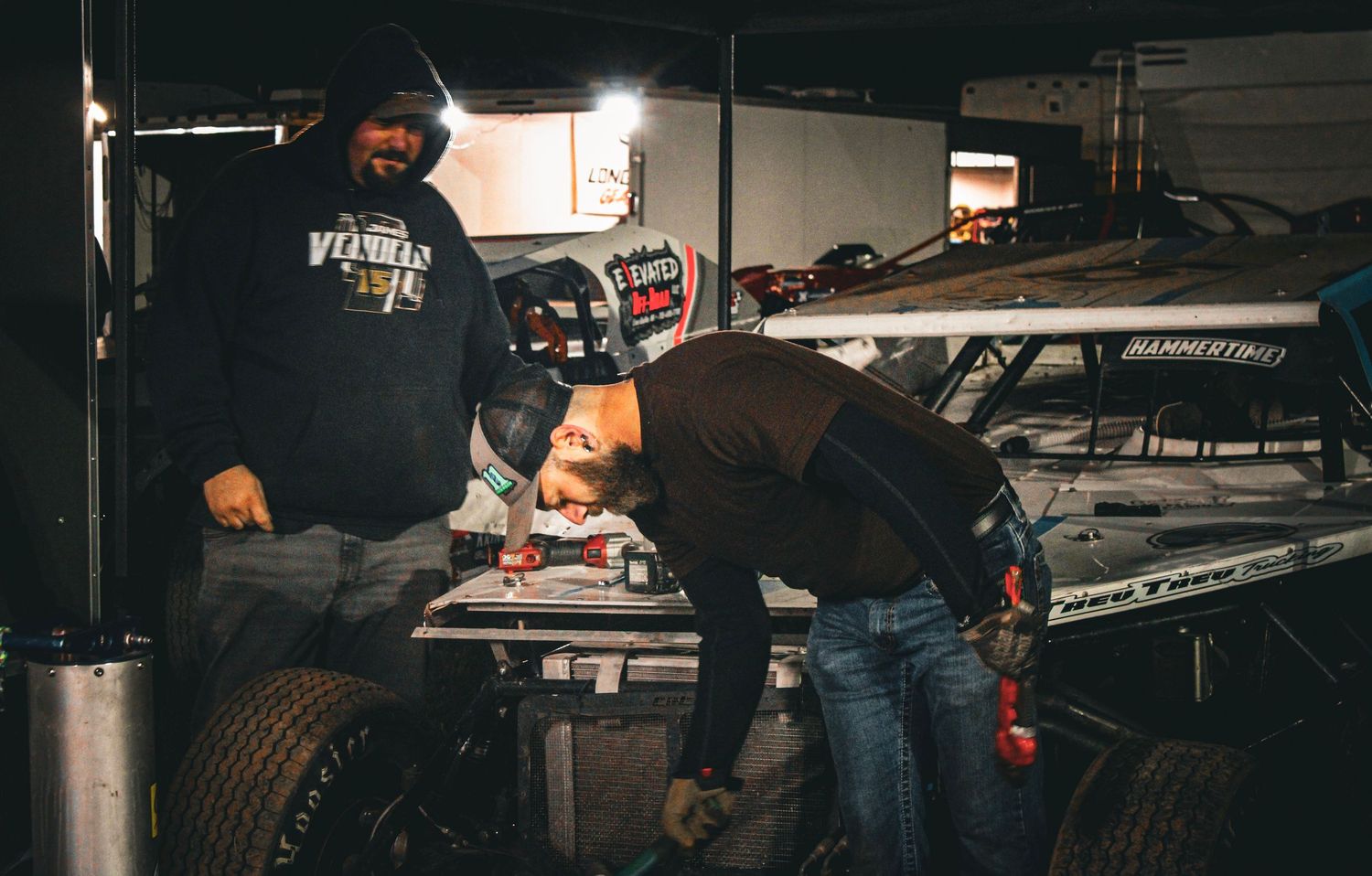 Team members performing maintenance work on racing vehicles in a garage environment.