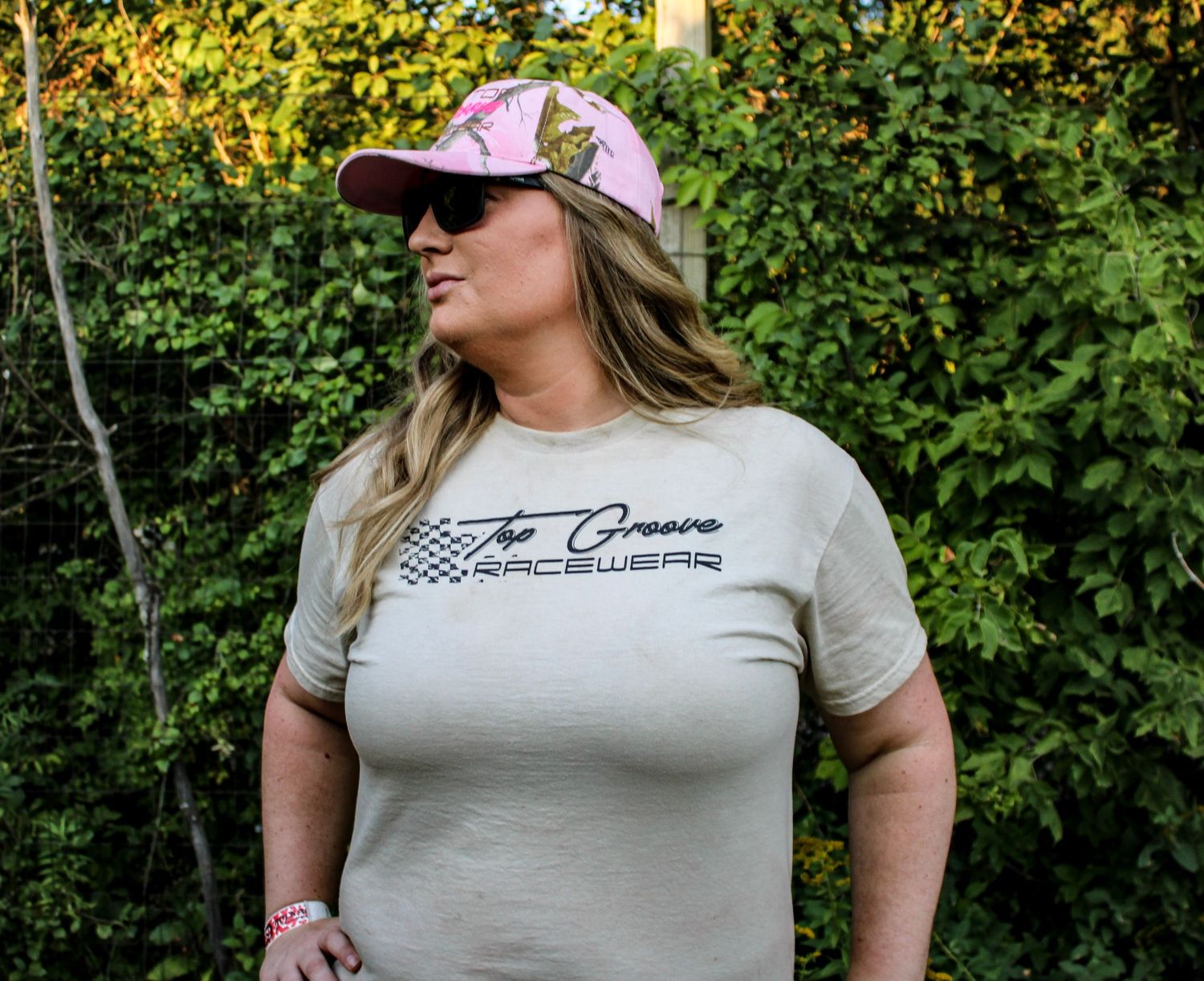 Woman wearing a cream colored t-shirt with custom graphics and pink cap outdoors.