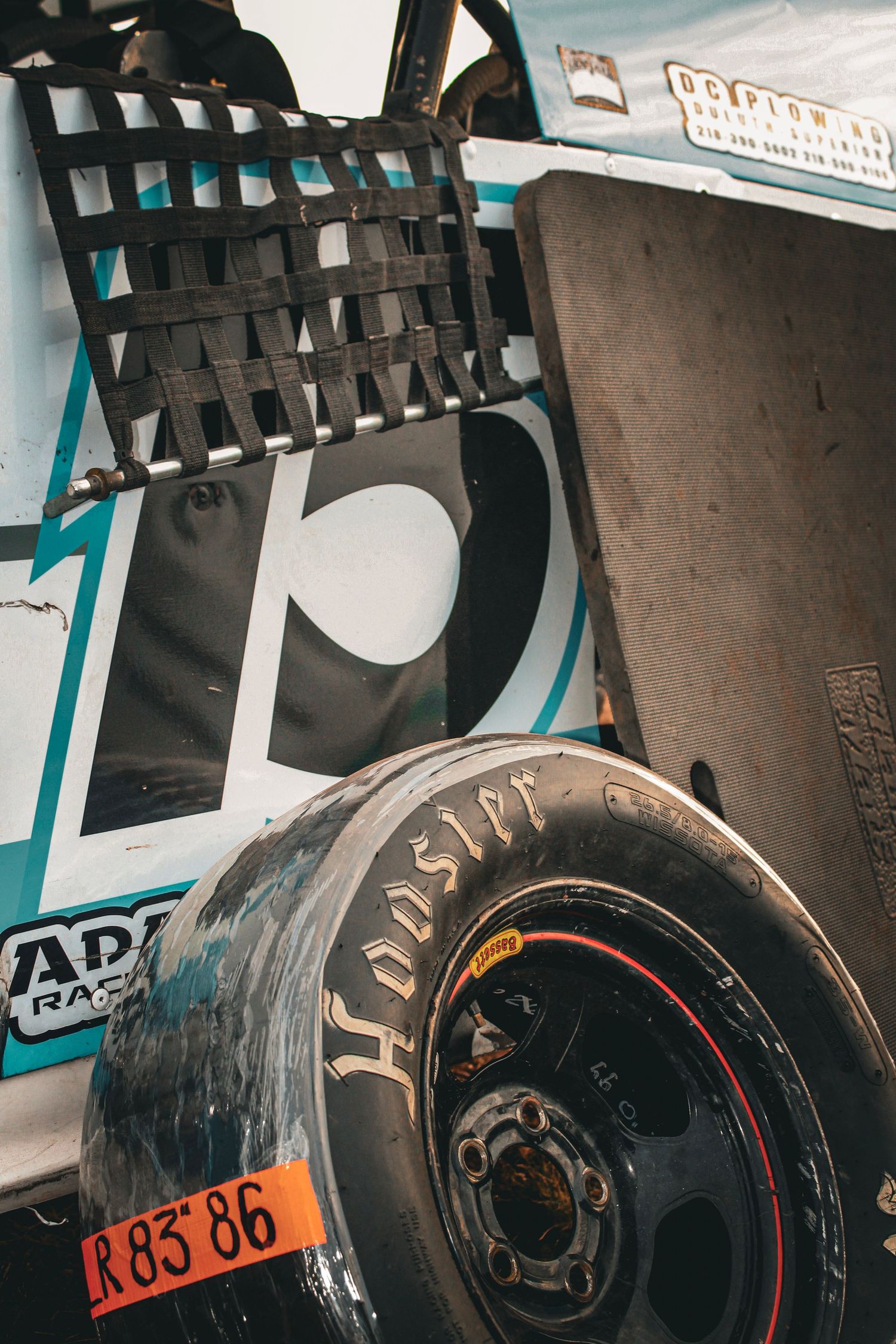 Close-up shot of used racing tires stacked against a wall with orange identification numbers.