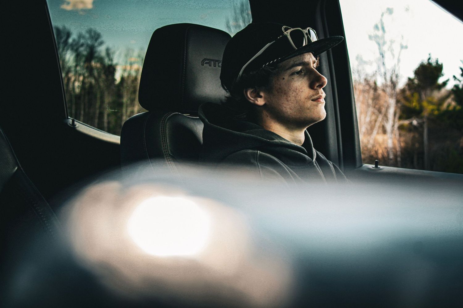 Man wearing sunglasses and cap sitting in a car seat, gazing out the window on a sunny day.