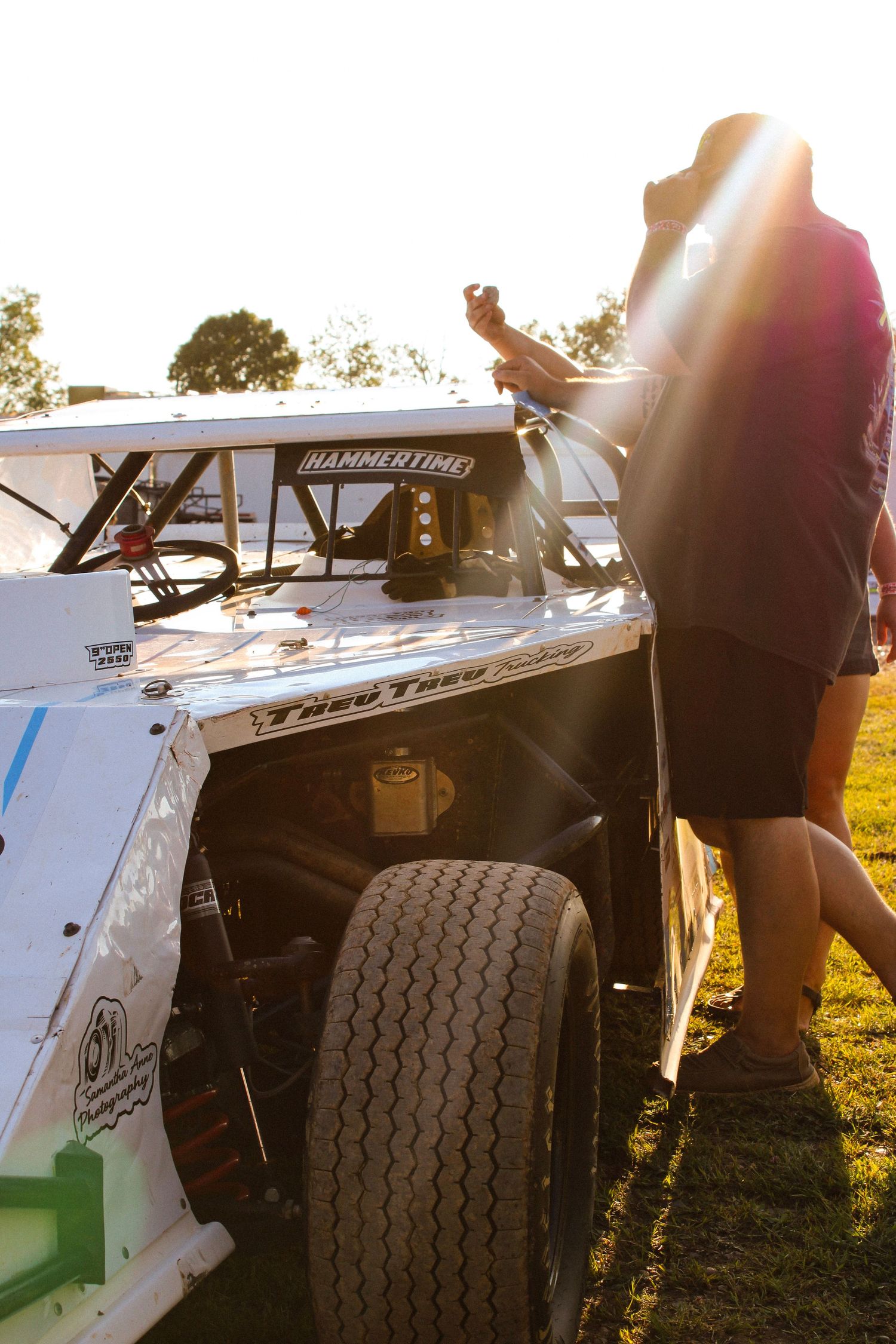 Racing team members inspecting car components during golden hour at the track.