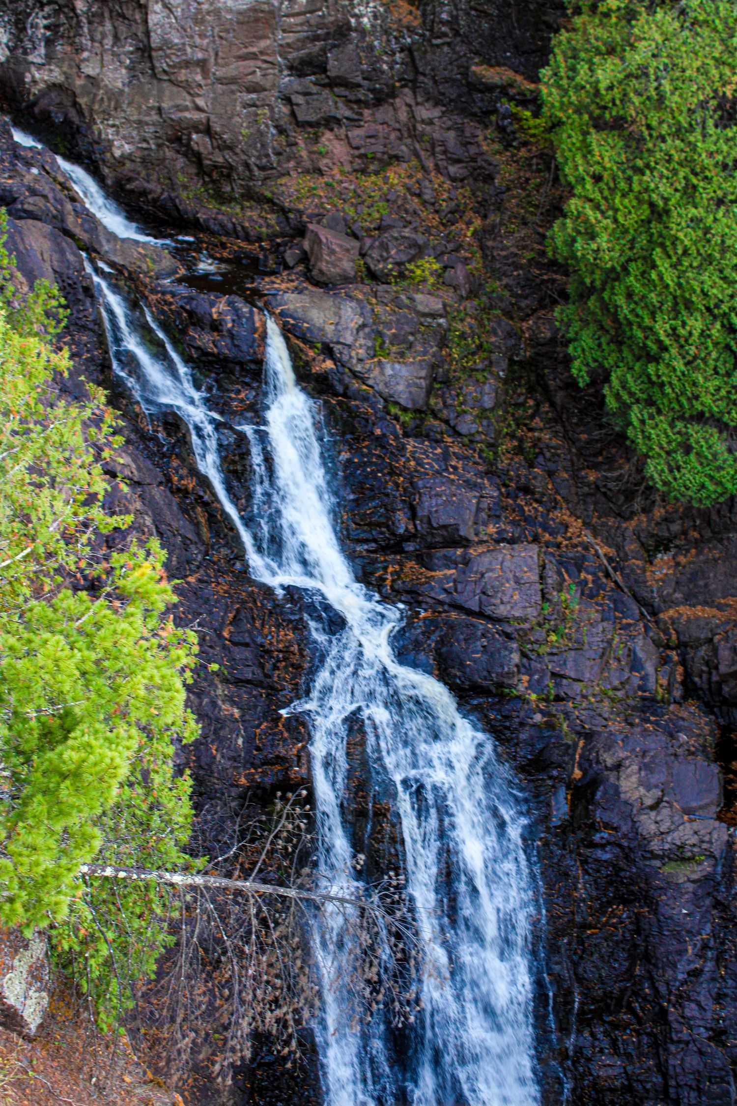 Majestic waterfall cascades down dark rocky cliffs surrounded by vibrant green vegetation.