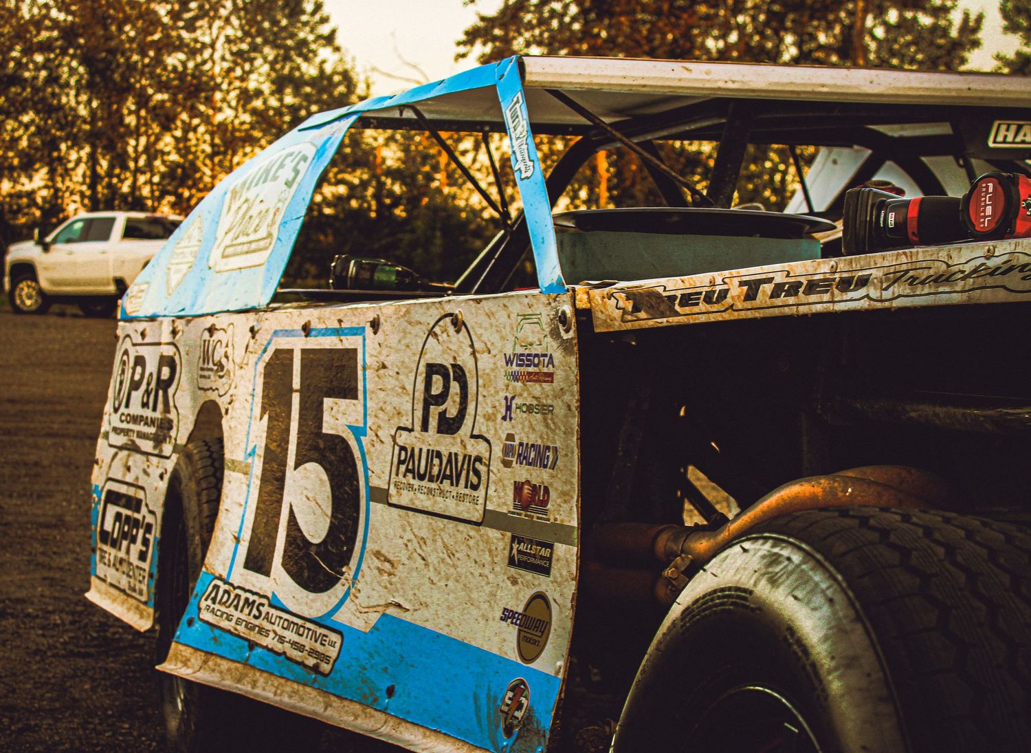A vintage race car with the number 15 painted on its side panel sits in warm evening sunlight.