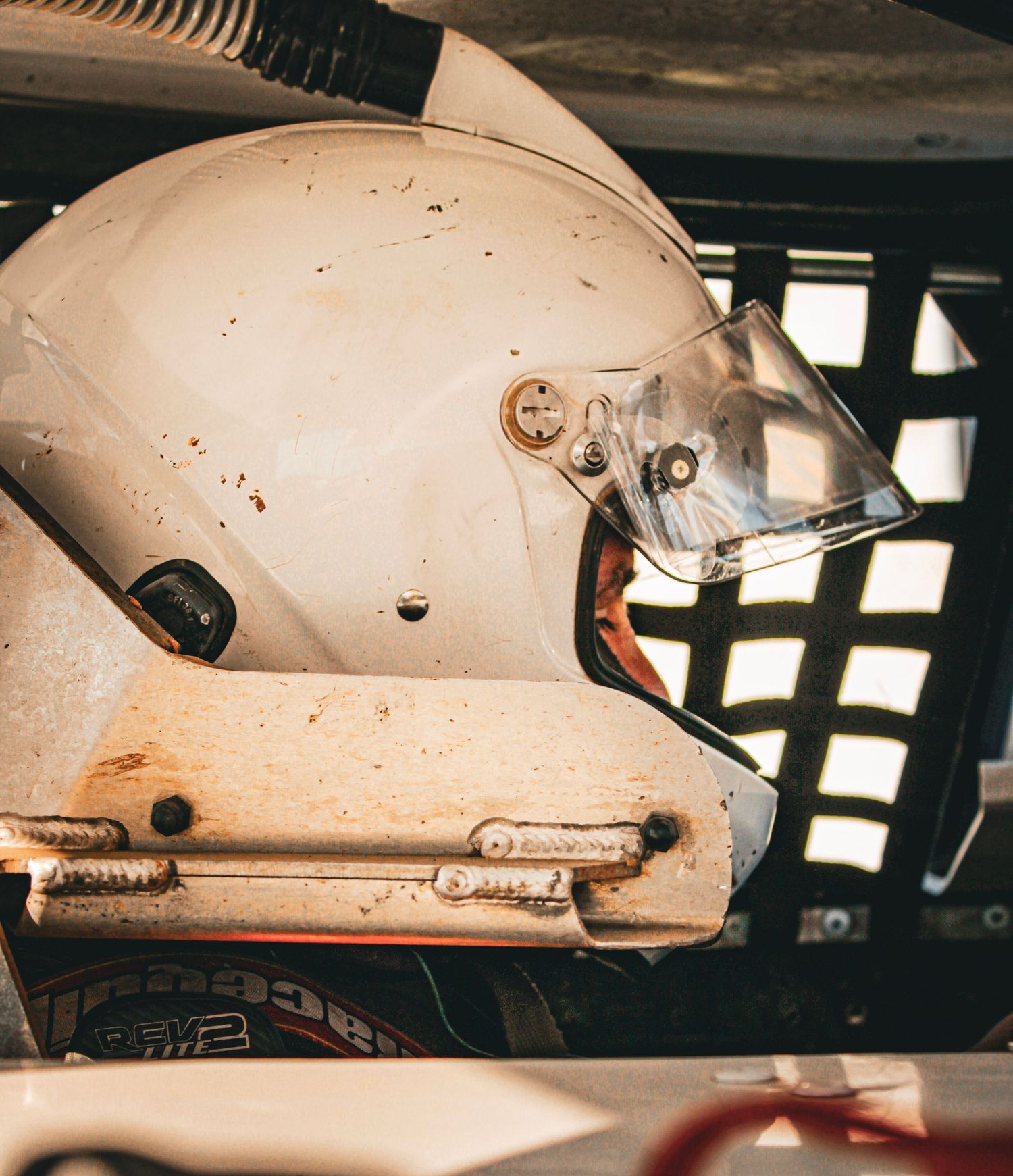 Close-up of a weathered white racing helmet with protective visor mounted inside vehicle.