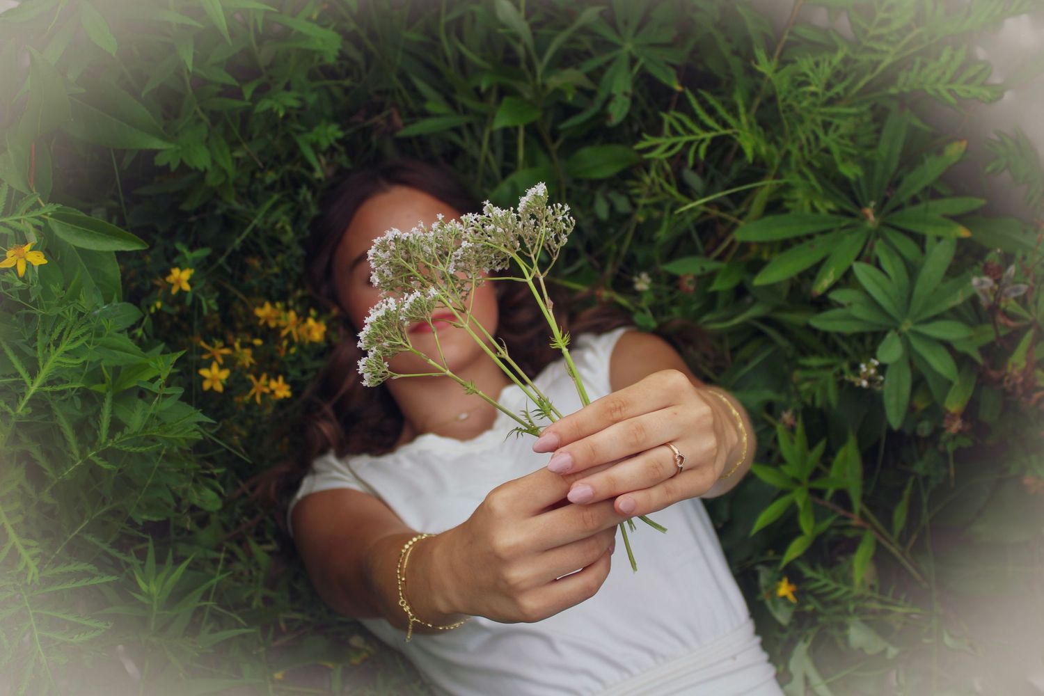 Woman holding white wildflowers in a lush green garden with yellow blooms in the background.