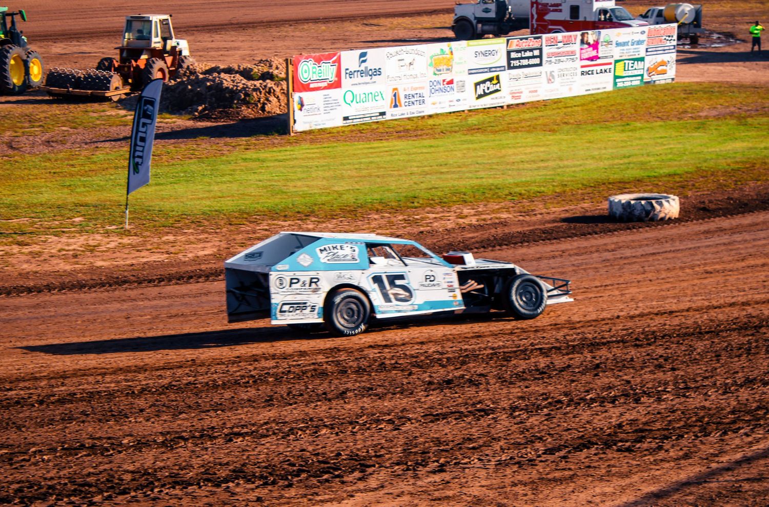 Race cars competing on a dirt track with advertising banners visible in the background.