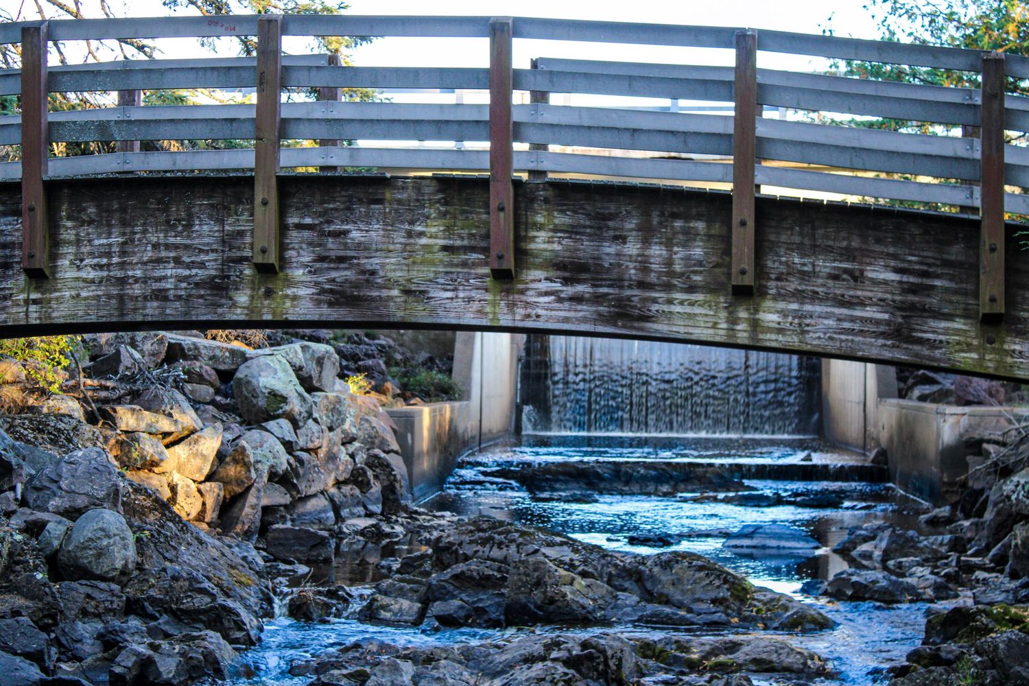 Stone bridge over rushing water with blue railings during daytime.