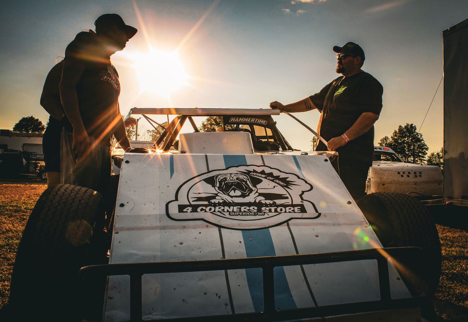 Racing team members working on car components during sunset at the track.