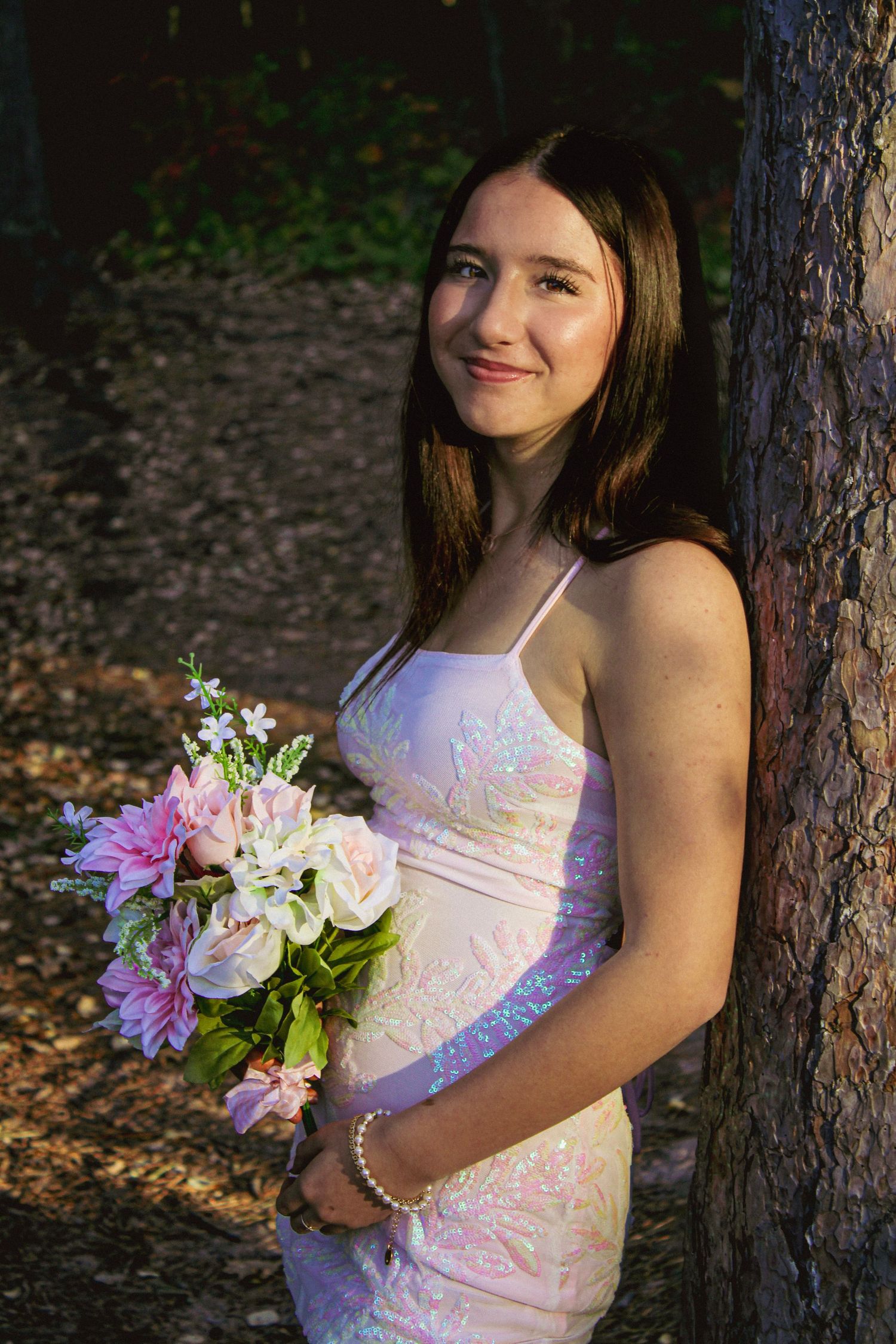 Pink floral bouquet held against a forest backdrop with pine trees.