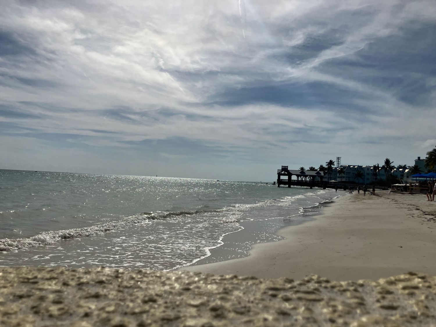 Panoramic view of a stormy beach coastline with dramatic cloudy skies and rolling waves crashing on the shore.