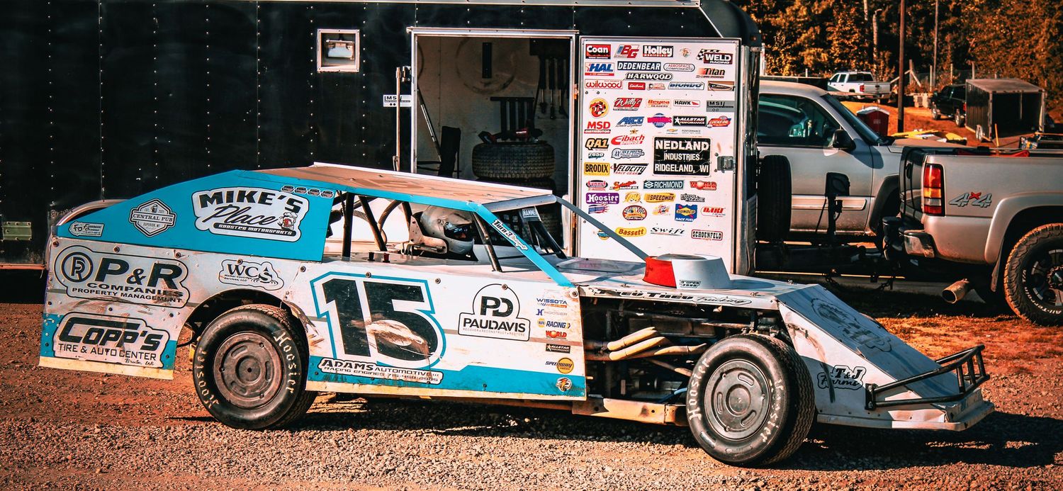 Blue and white number 15 dirt track race car parked in pit area.