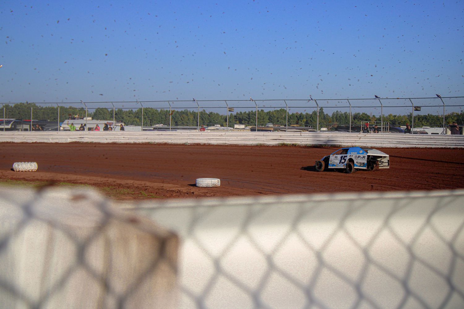 Wide panoramic view of a dirt race track with white barriers and fencing.