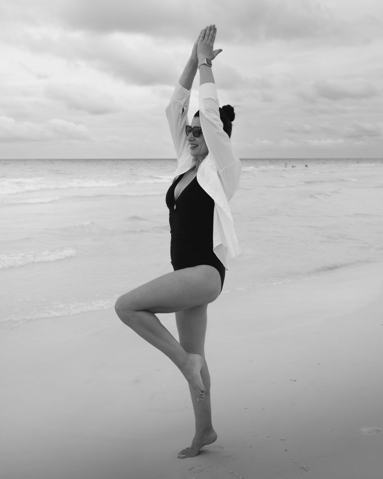 Artistic black and white photos of beachgoer in swimwear striking dynamic poses on sandy shore.