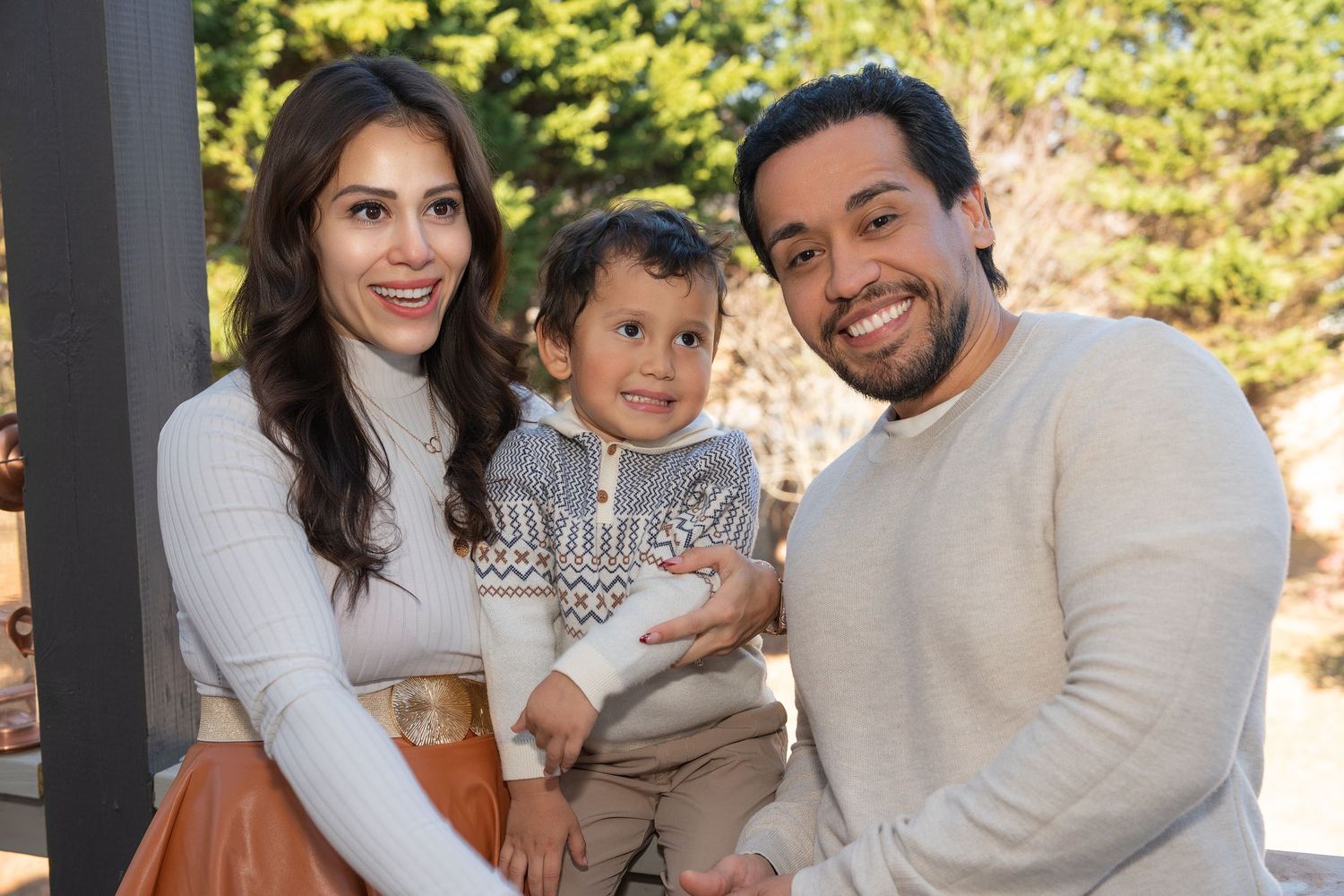 Family wearing white and beige outfits sitting together and smiling during outdoor photo session.