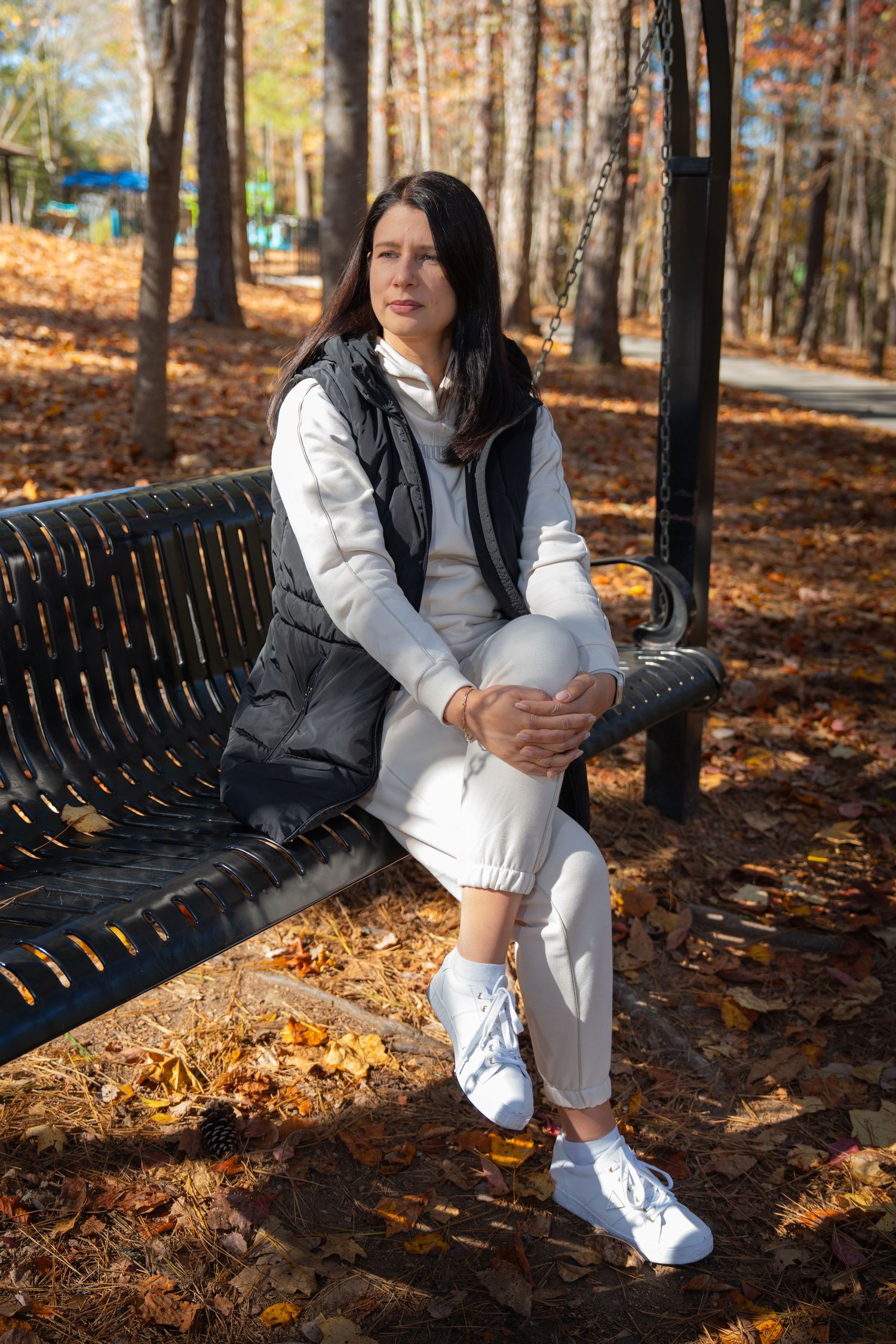 Person in white athletic wear sits on park bench surrounded by fall leaves.