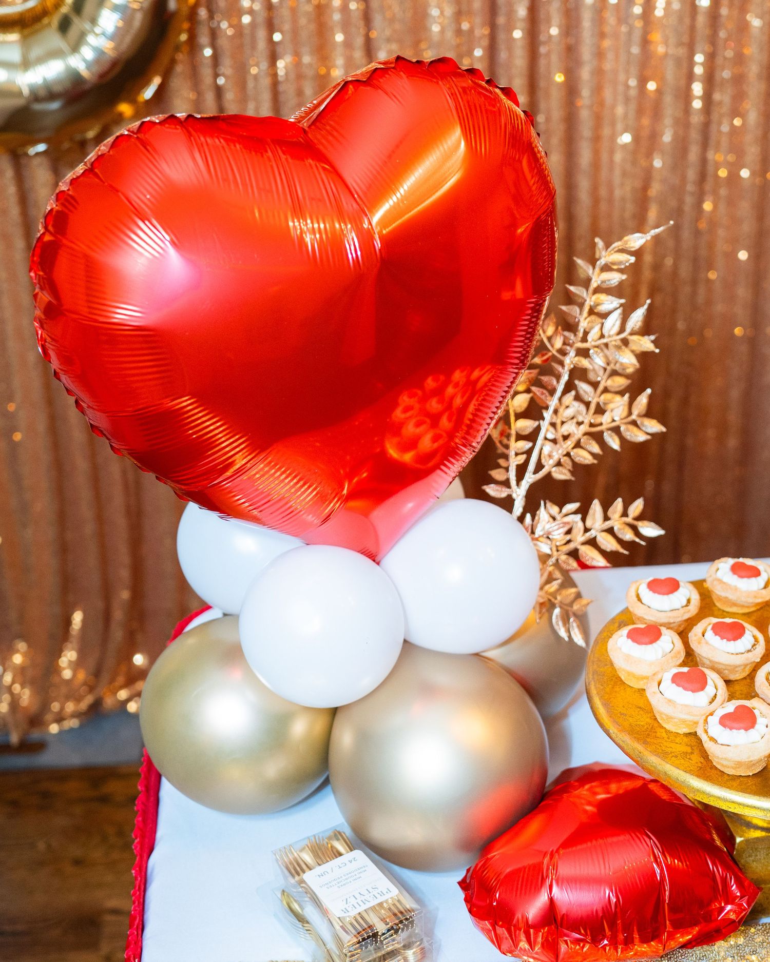Red heart balloons and silver ornaments create an elegant Valentine's Day party decoration against a sparkly backdrop.