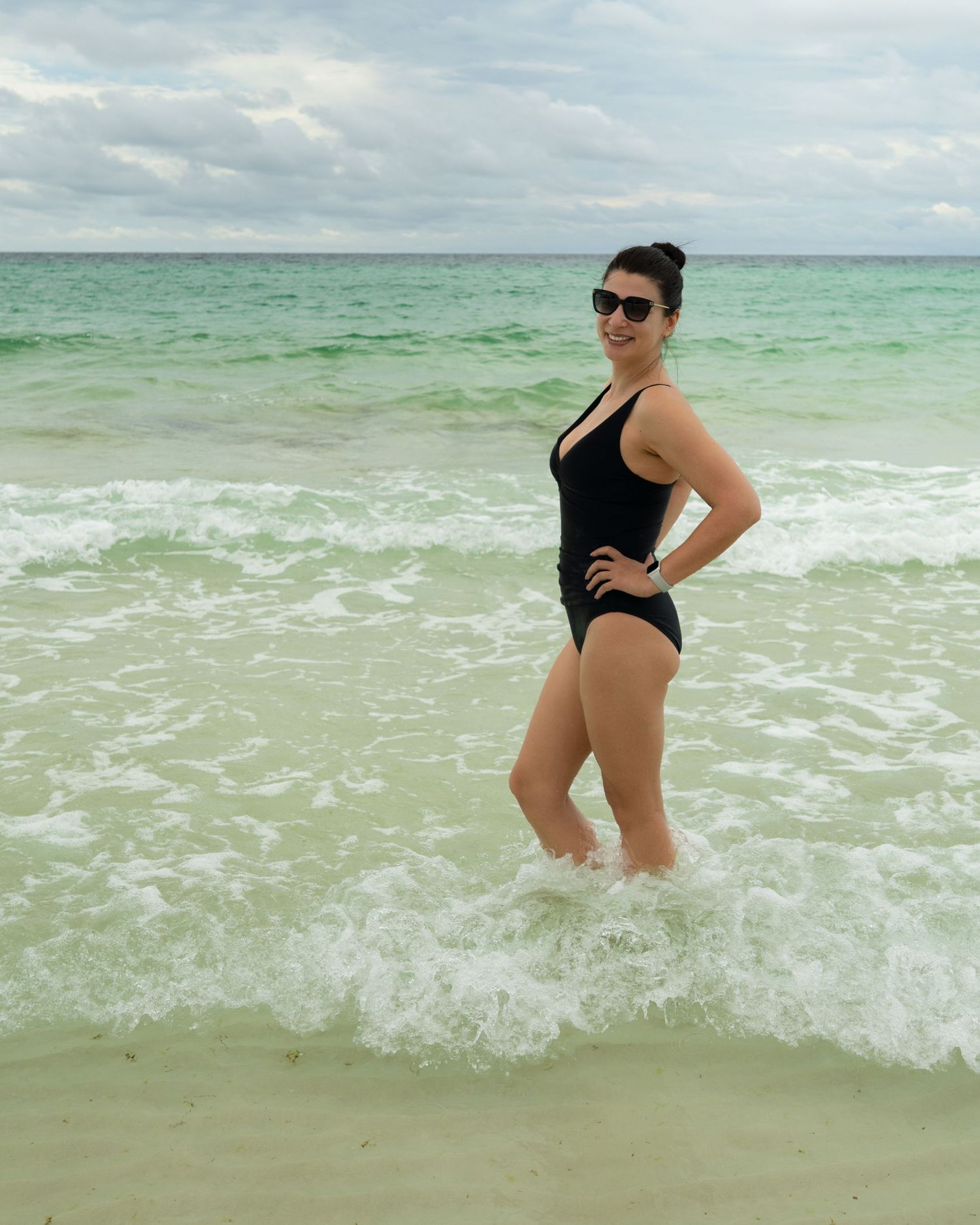 Person wading in crystal clear turquoise ocean waters wearing black swimsuit.