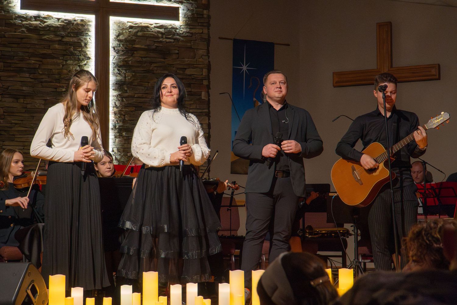 Musical ensemble performs in front of stone wall with crosses and candles.