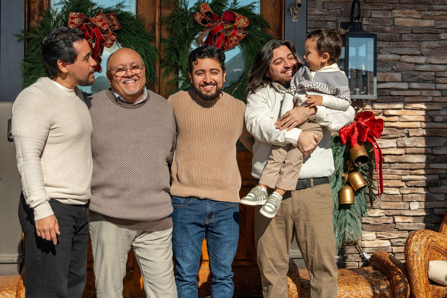 A group stands together on a front porch decorated for the holidays with pumpkins and festive greenery.