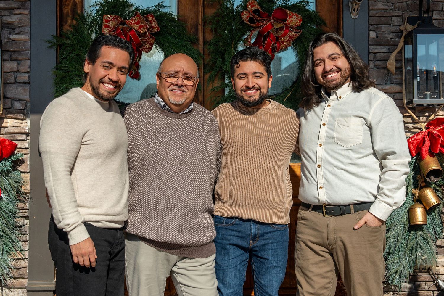 Family members stand together in coordinated beige and white sweaters for a festive holiday portrait.