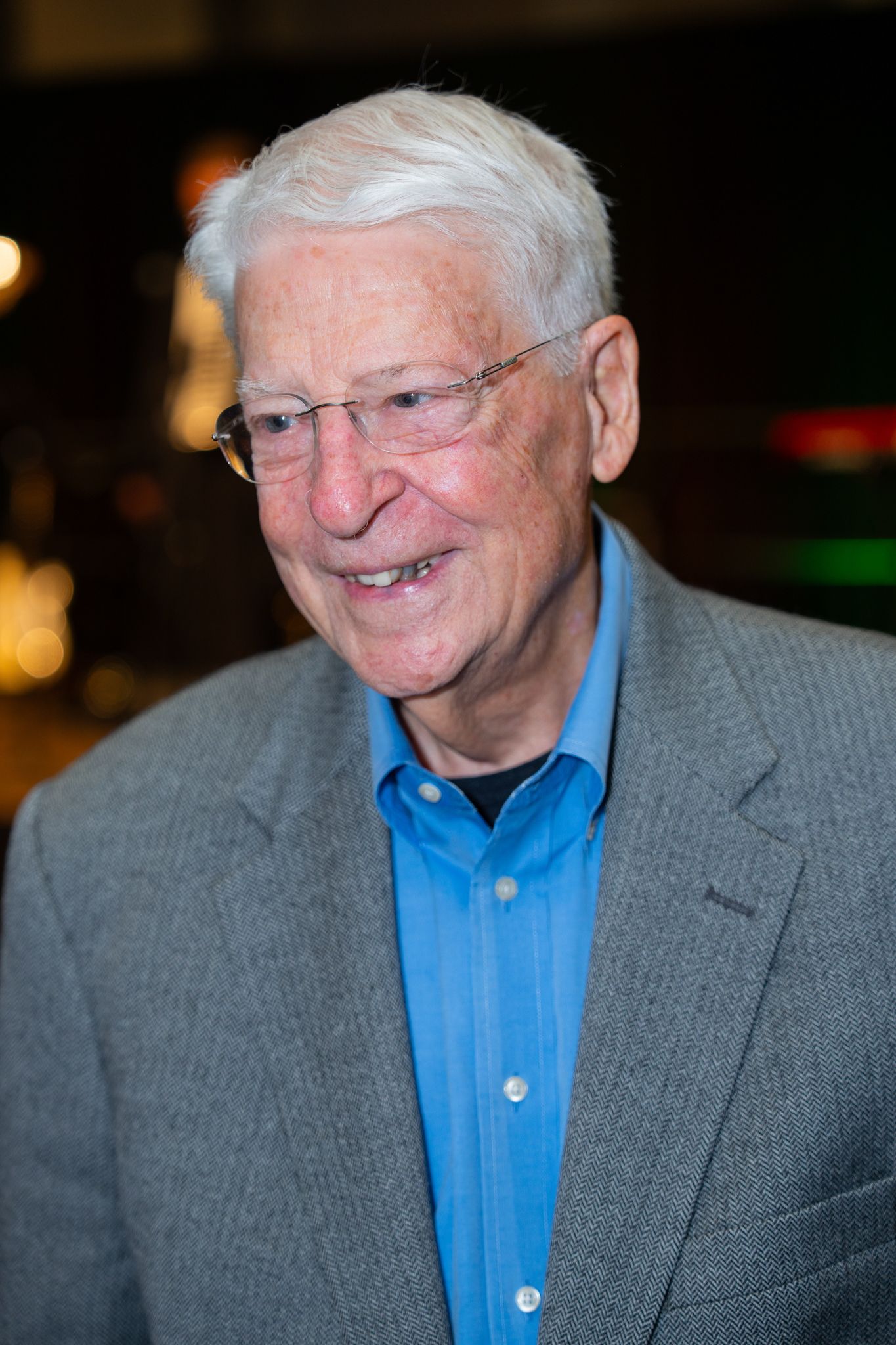 Person in gray suit and blue shirt smiling at evening event.